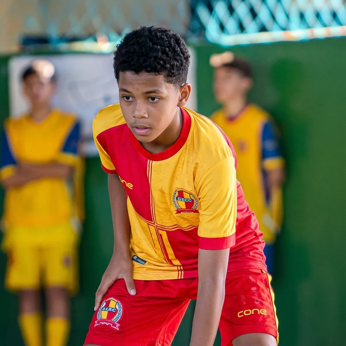 Atleta da ADEC com uniforme vermelho e amarelo se preparando para dominar a bola na quadra